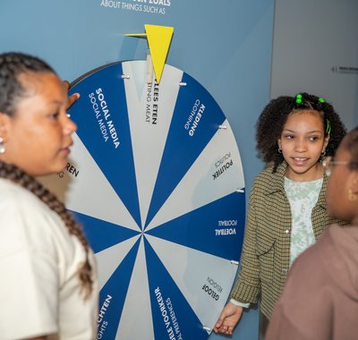 Een groepje kinderen staat rondom een wiel met stellingen waaraan gedraaid kan worden.